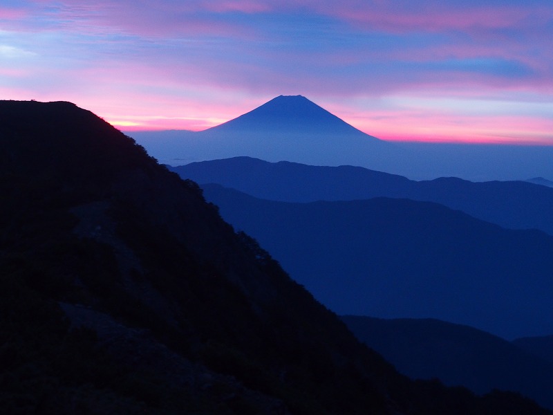 県営光岳小屋から望む富士。朝焼けでピンクに染まる雲をキャンバスにシルエット状に浮かび上がる雄大な富士山が美しい。左手の山はイザルガ岳です。