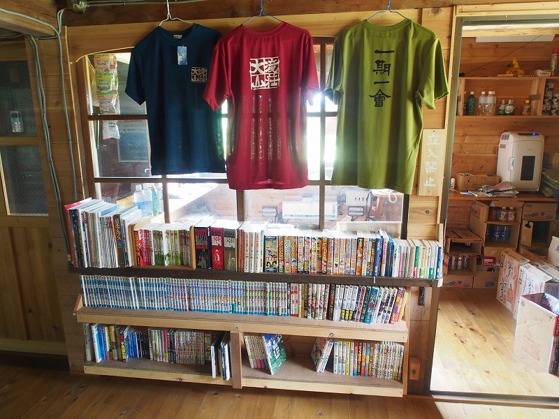 三色のオリジナルTシャツ。各種漫画の単行本、山岳関係の本が置かれています。