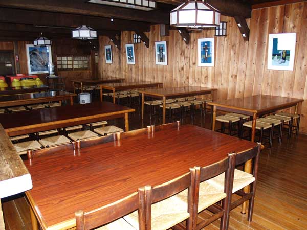 食堂。約100人が一度に食料とることができる大きな食堂。壁には、絵画や版画が飾られ、クラシカルな趣を醸し出しています。食後にはオーナーの赤沼健至氏による名物のアルペンホルン演奏タイムです。奥のスペースには自炊専用のテーブルが置かれています。