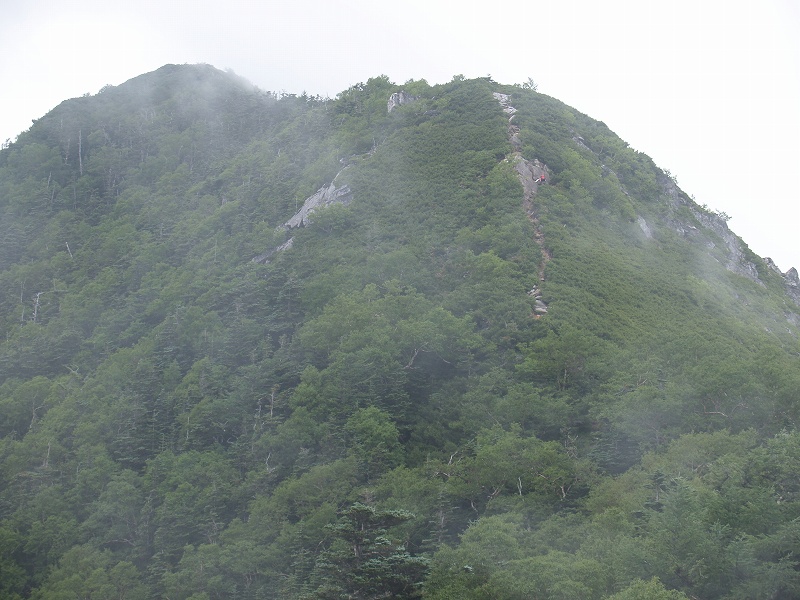 前の写真位置から高嶺を望遠で撮影 。左上が高嶺で、山頂近くは岩場となっています。右上のピーク近くに登山者が小さく見えます。