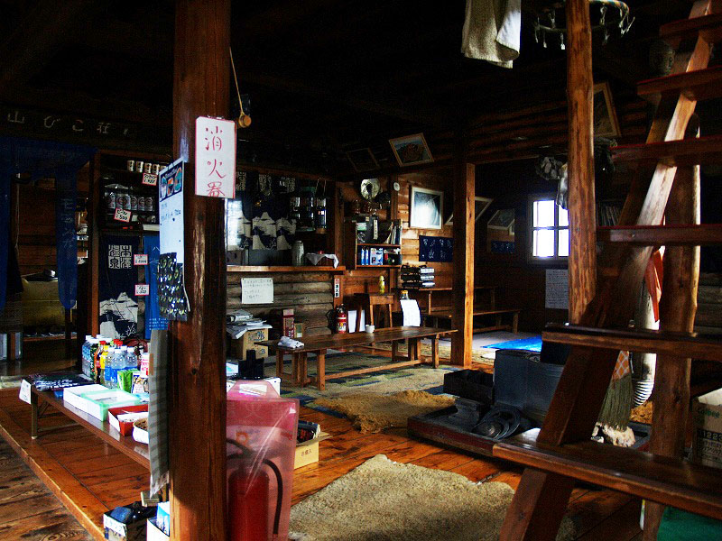 山彦荘の一階の様子　薪ストーブとランプが置かれた食堂兼談話室になっています。２階にカイコ棚式大部屋があるのみで個室はありません。
